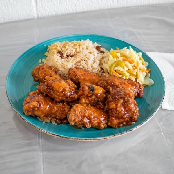 A teal plate with brown stew chicken, rice and peas, and coleslaw, with a fork on a napkin.