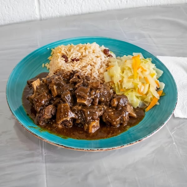 Oxtail stew with rice and peas, and steamed cabbage on a blue plate.
