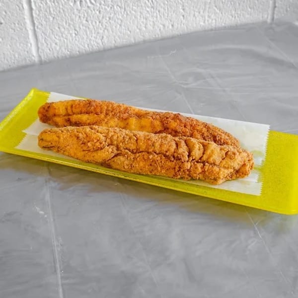 Two crispy fried fish fillets on a yellow rectangular plate with white paper lining.
