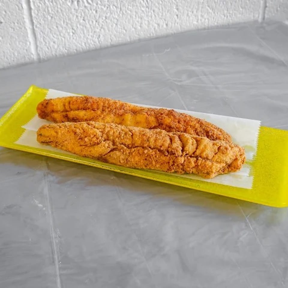 Two crispy fried fish fillets on a yellow rectangular plate with white paper lining.