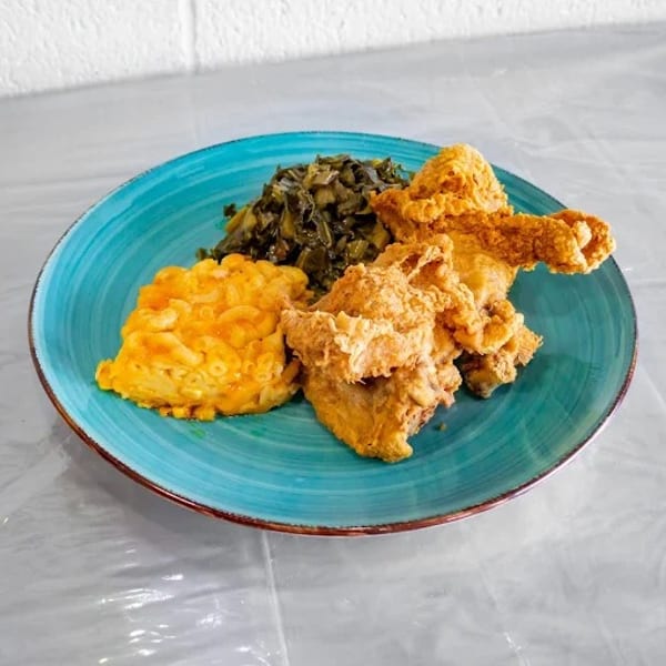 Fried chicken, macaroni and cheese, and collard greens on a teal plate.