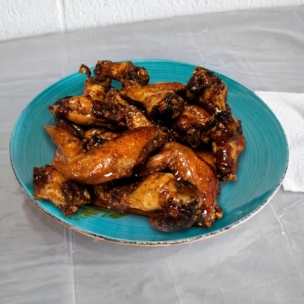 A blue plate filled with glistening, saucy chicken wings, with a fork and napkin beside it.