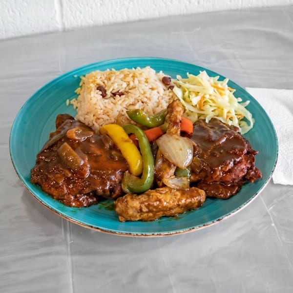 A vibrant plate of Jamaican brown stew chicken, rice and peas, and coleslaw on a blue plate.