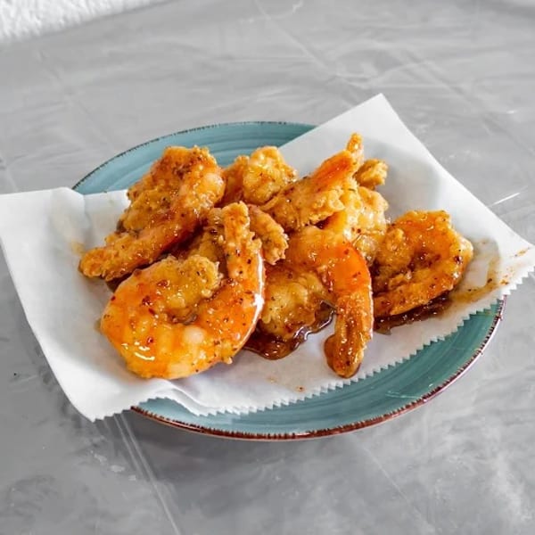 A plate of crispy fried shrimp coated in a sweet and spicy sauce, served on white parchment paper.