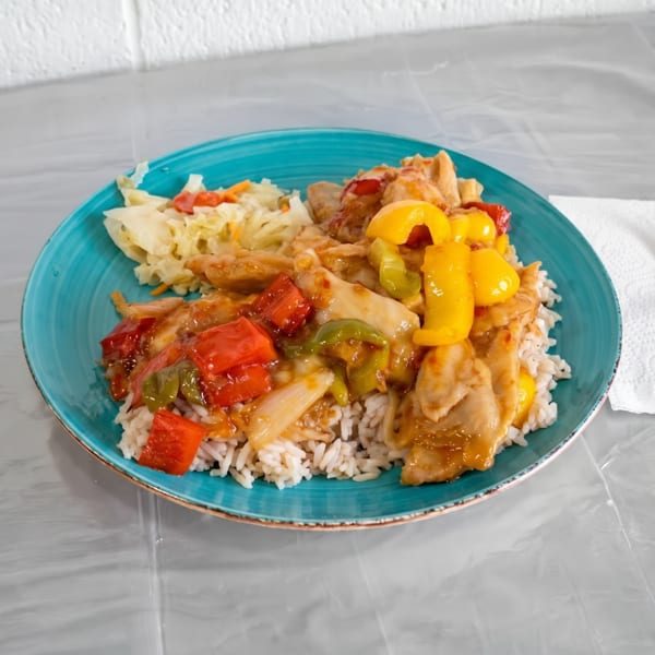 Sweet and sour chicken with rice and cabbage salad on a blue plate.