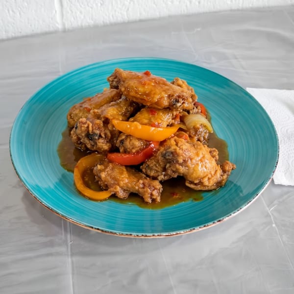 Sweet and sour chicken wings with bell peppers and onions on a blue plate.