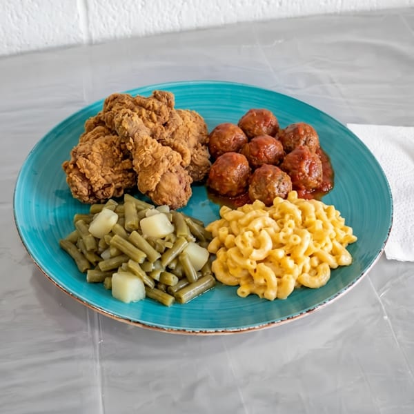 A blue plate with fried chicken, meatballs, green beans with potatoes, and macaroni and cheese.
